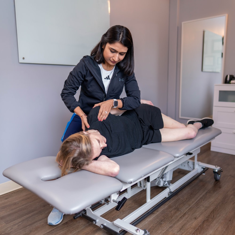 A patient lies on her side while a therapist palpates her shoulder